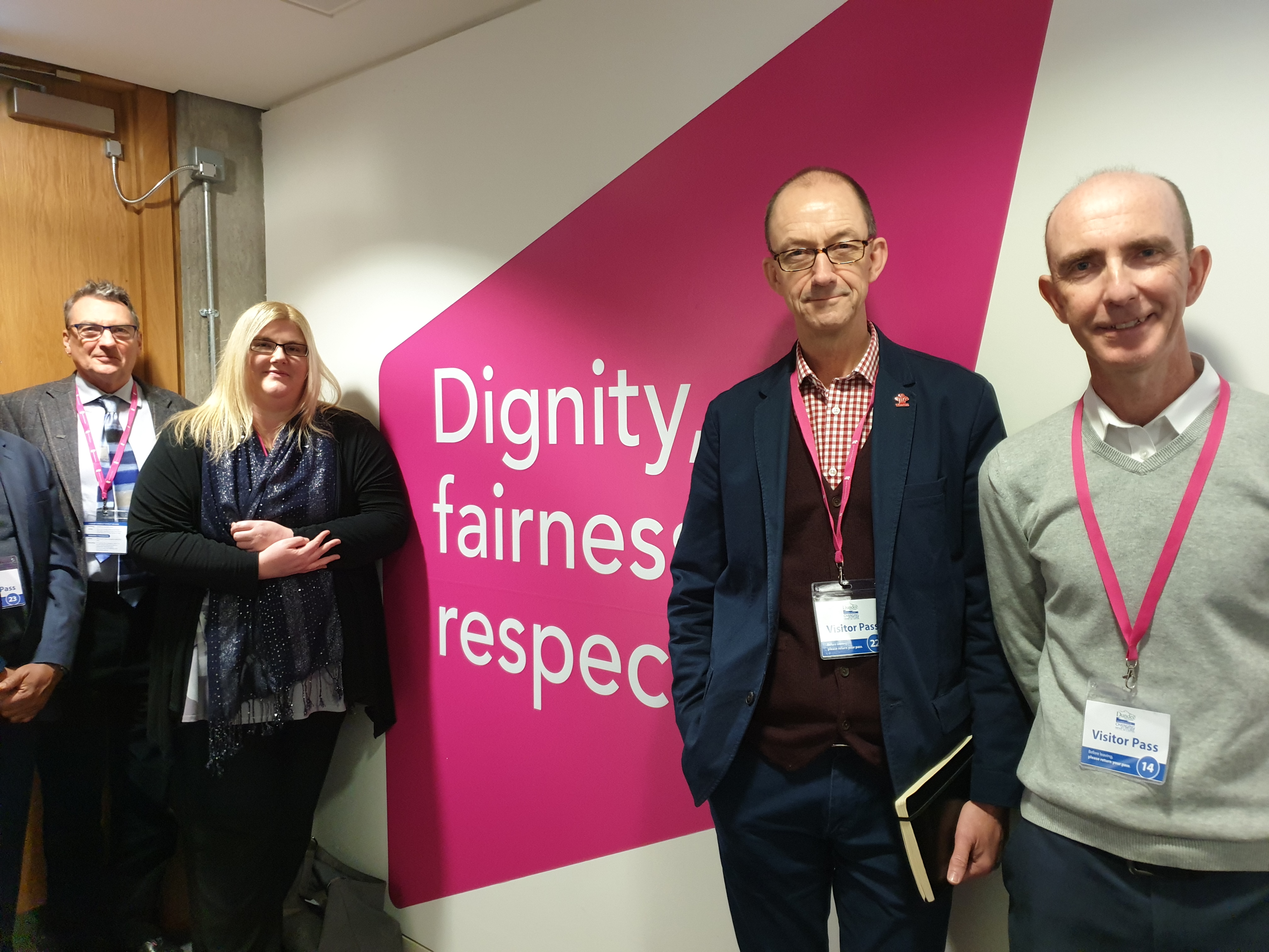 SSAC members on a visit, standing in front of sign which says Dignity, fairness, respect.