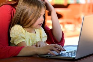 Parent working on laptop at table with child sitting on lap 